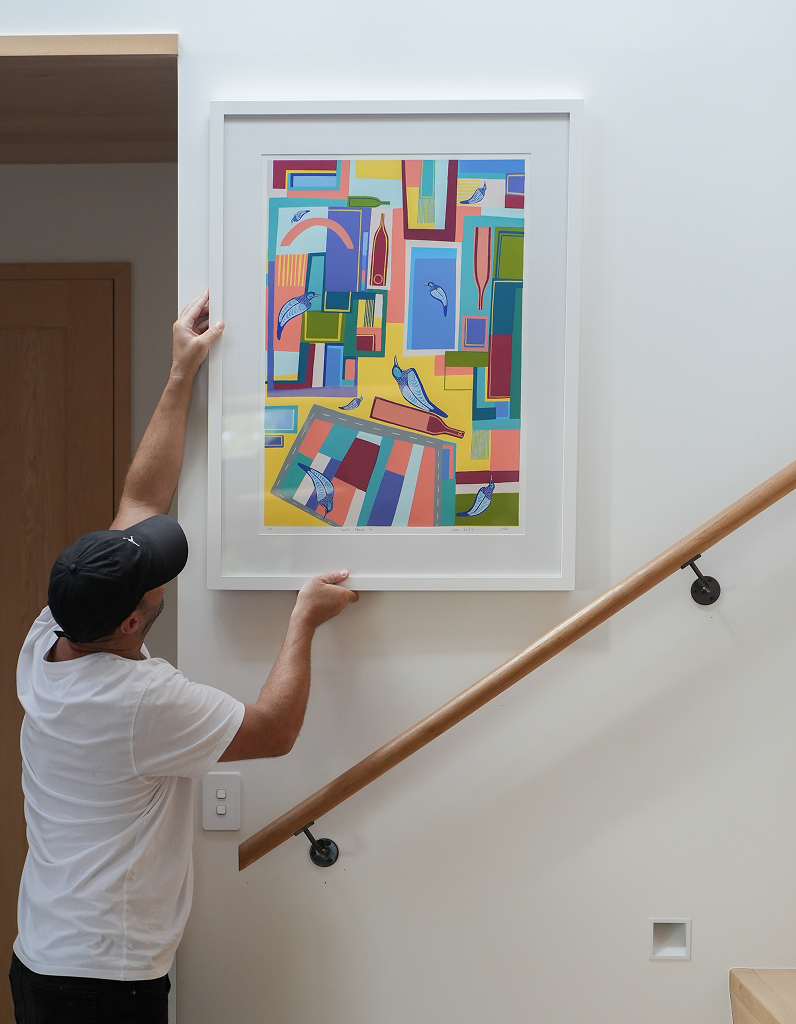 Sam Leitch hanging a colourful abstract screen print on a wall