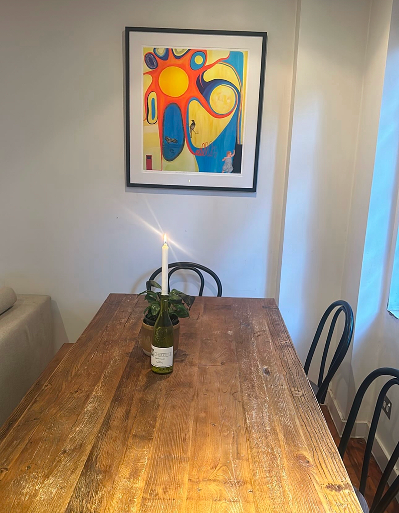 Wooden dining table with a candle and plant, colorful abstract art on the wall.